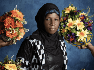 A woman in checker print dress surrounded by bouquets of flowers. 