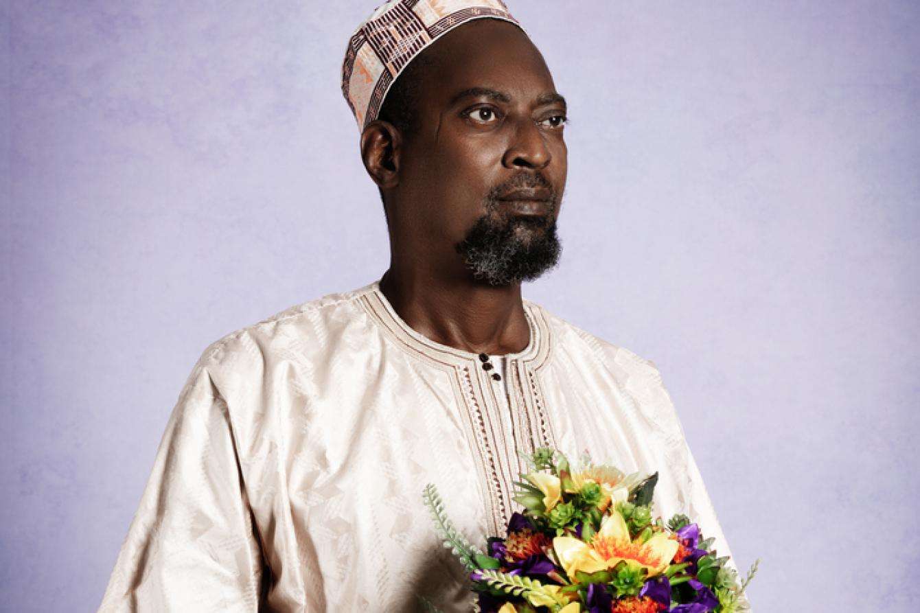 A man in white holding bouquet of flowers against purple background.