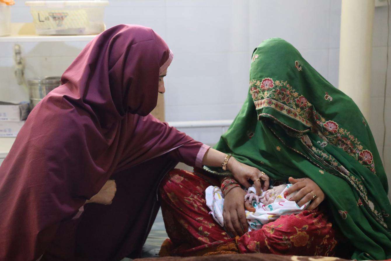 A health worker checks a baby held in its mother's lap in Kuchlak, Pakistan.